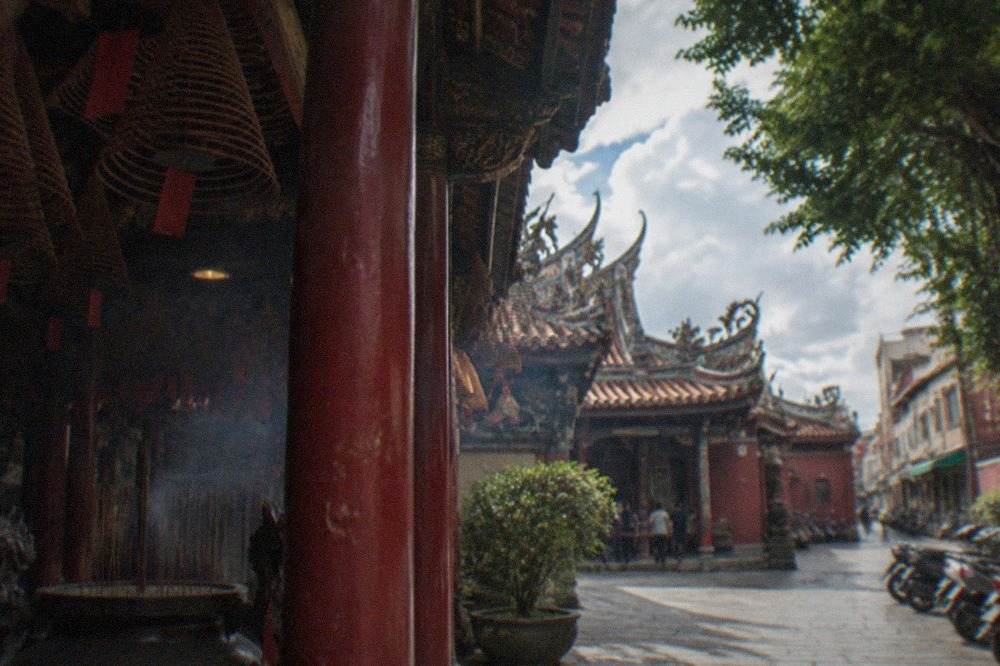 A historic Taiwanese temple courtyard with red walls, ornate roof decorations and stone paving in daylight