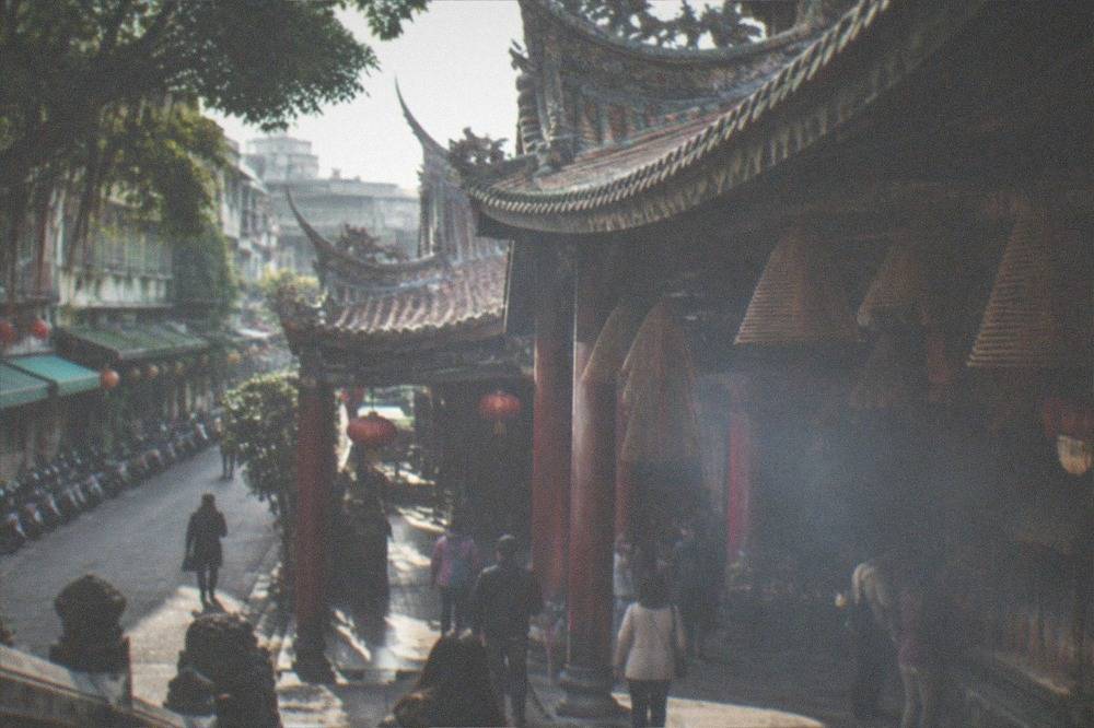 Worshippers and visitors moving through a busy Taiwanese temple hall with lanterns and incense coils