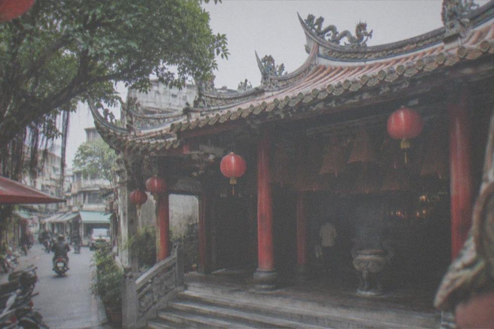 Morning light falling on a temple entrance with stone steps, red pillars and hanging plaques