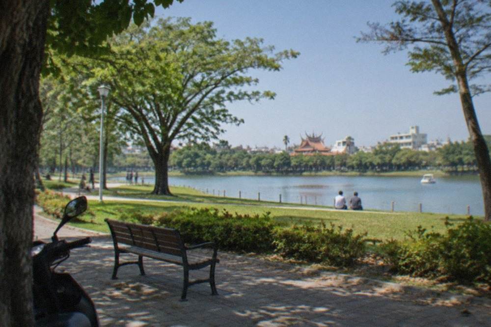 A wide public park in Tainan with open lawns, trees and a lake under a blue sky