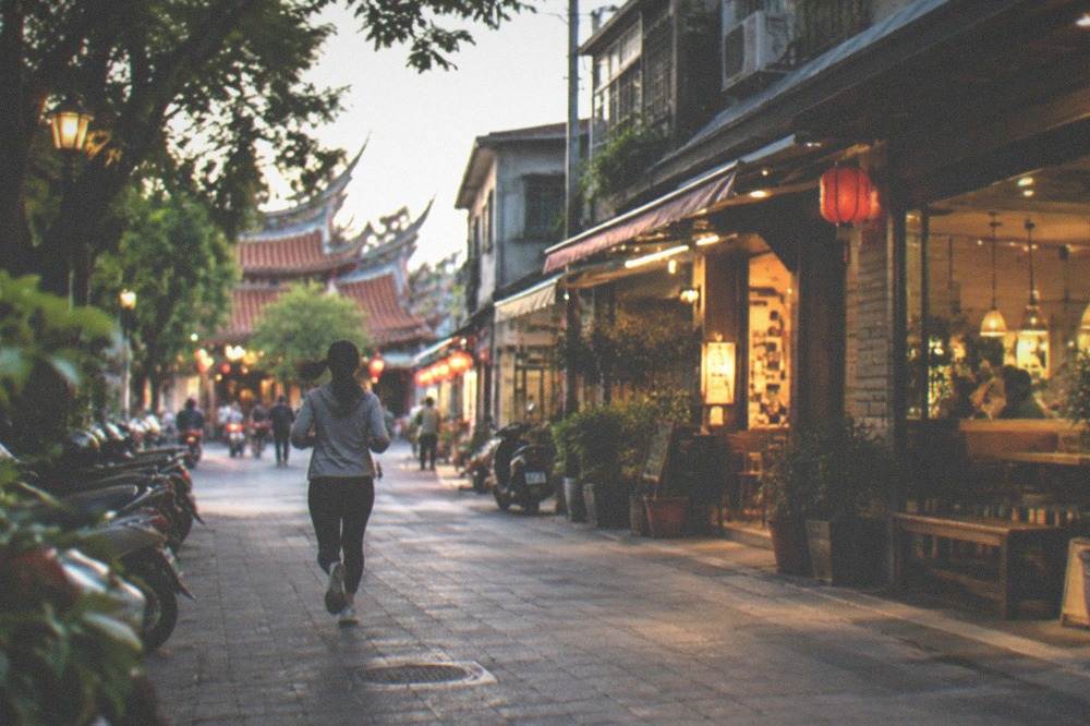A shopping and dining complex beside a park at dusk with lit storefronts