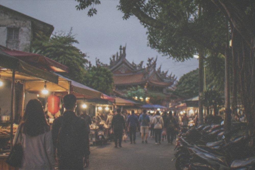 A crowded night market aisle lit by warm stall lights at dusk