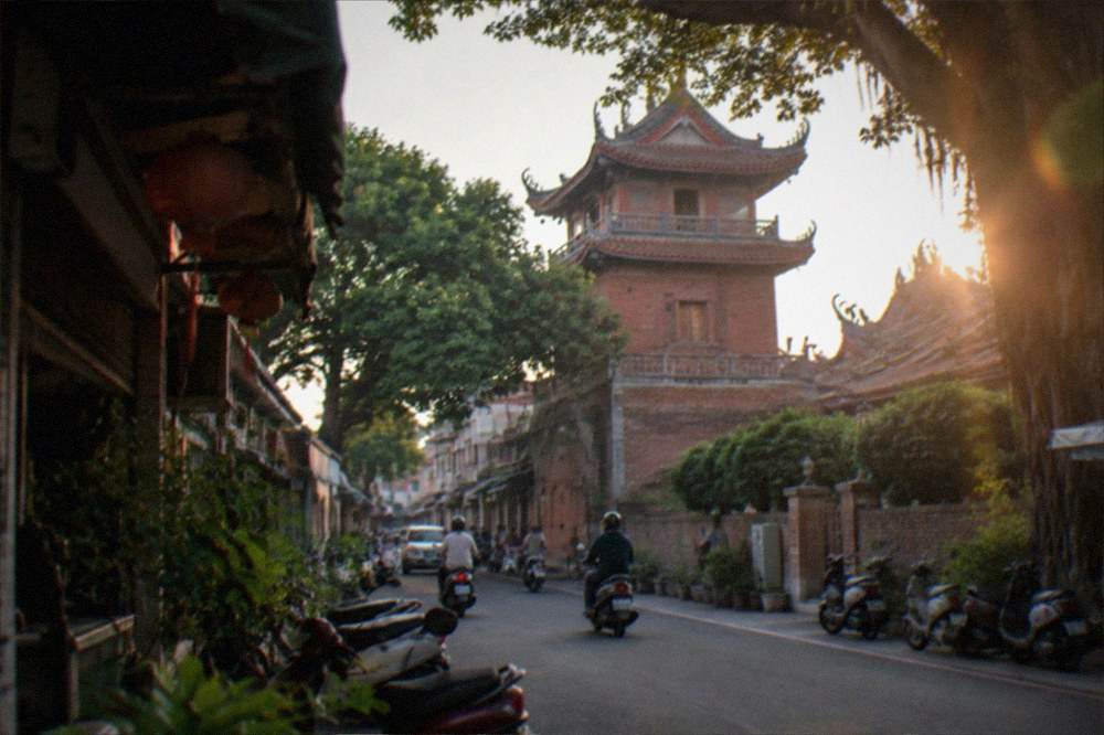 A historic red-brick tower with Chinese pavilion roofs lit in the early evening