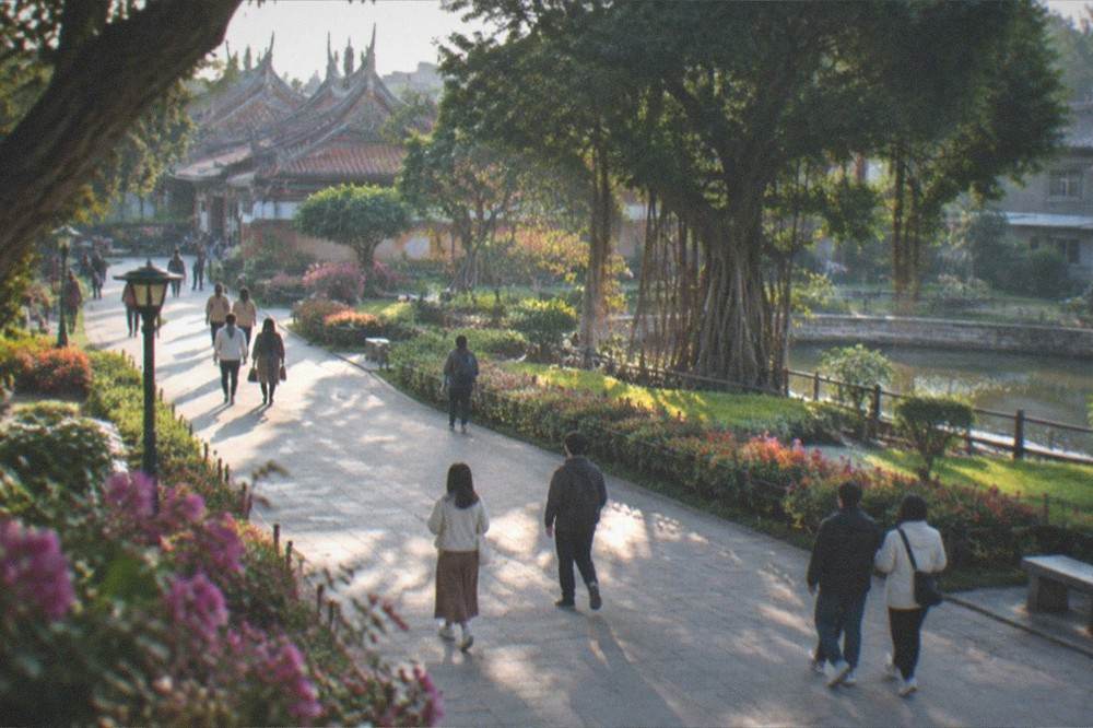 People strolling on a wide park path between flower beds in late afternoon light