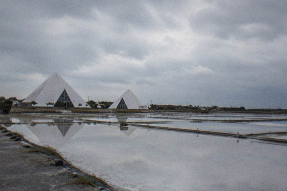 Rows of shallow rectangular evaporation pans filled with pale brine reflecting the sky