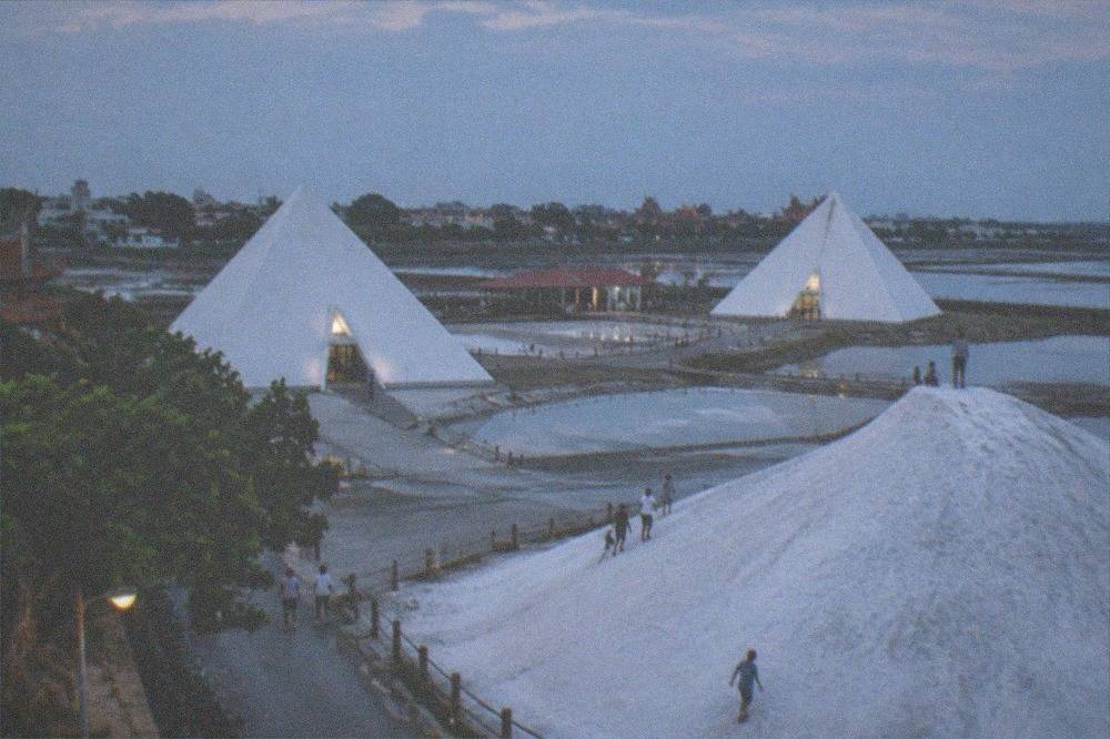 A tall white mound of crystallized salt rising above flat ground with visitors on its slope