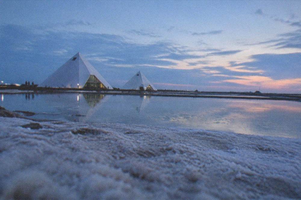A wide coastal panorama with white salt ground, still water and a wide open sky