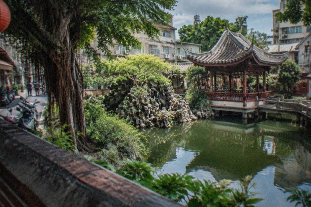 A quiet classical Chinese garden in Tainan with a pond, a curved pavilion and old banyan trees