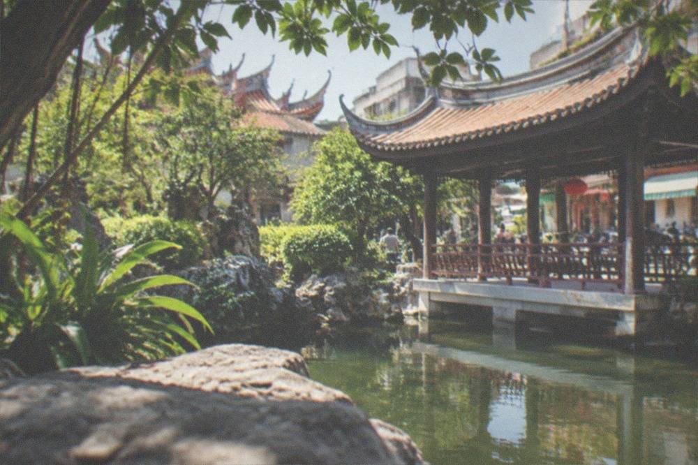 A curved pavilion beside water in a Tainan garden, framed by trees