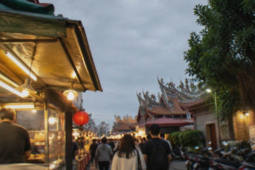 Crowded aisle of a Tainan night market at dusk with food stall lights overhead