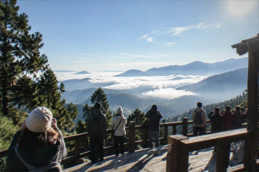 Tourists gathered on a wooden sunrise viewing platform above layered mountain ridges