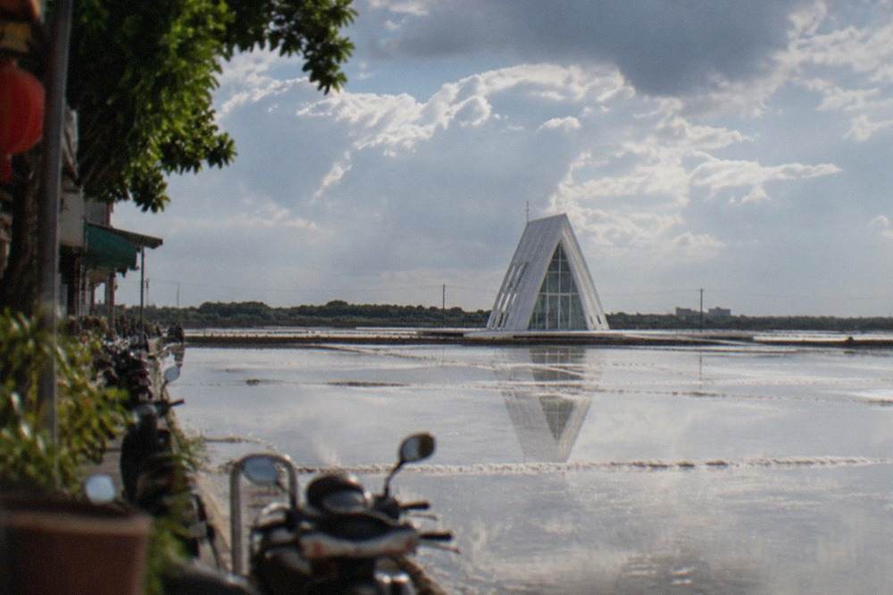 A white crystal-shaped chapel building standing on flat reflective salt flats along Taiwan's southwest coast