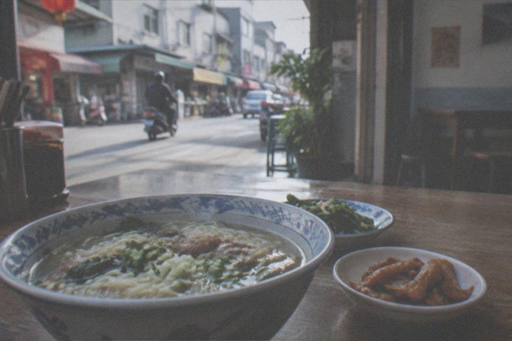 A bowl of noodles and small side dishes on a wooden table at a Taiwanese eatery