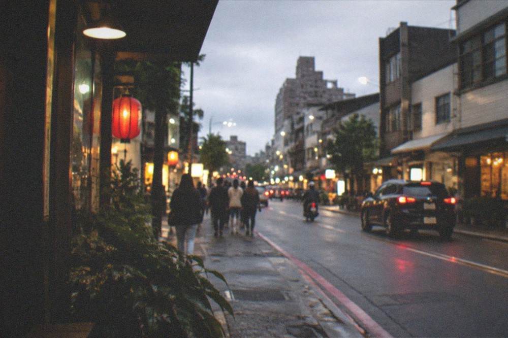 Dusk falling over a Taiwanese city street with lit shopfronts and people walking