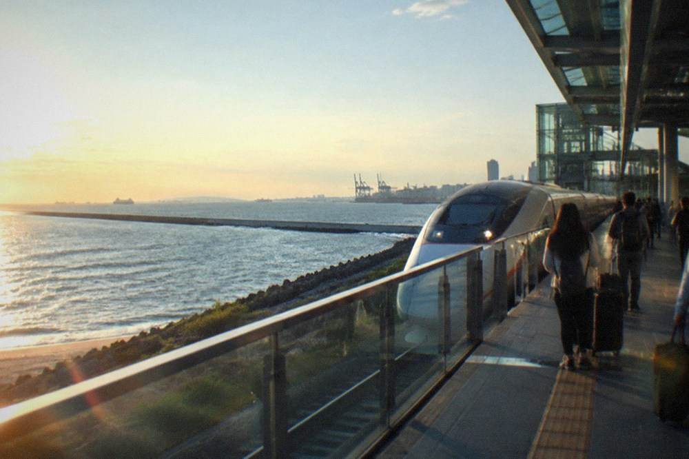 A high speed train stopped at a modern glass station platform with travelers waiting with luggage