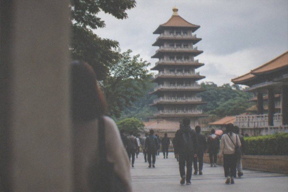 Visitors walking along a wide paved path toward a large pagoda at a monastery complex