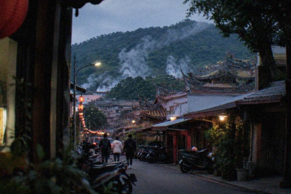 A hillside town street with shops and steam drifting above the rooftops