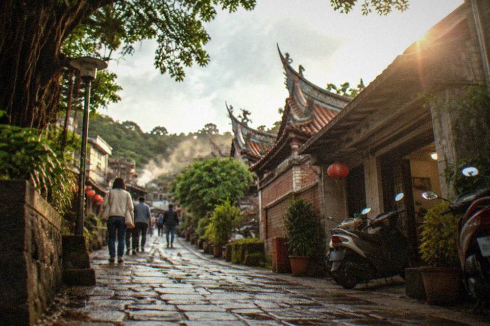Visitors walking a stone path between hot spring hotels in a green hillside valley