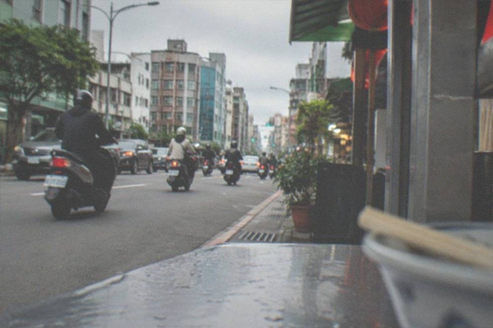 Busy daytime street in a Taiwanese city with shops and scooters