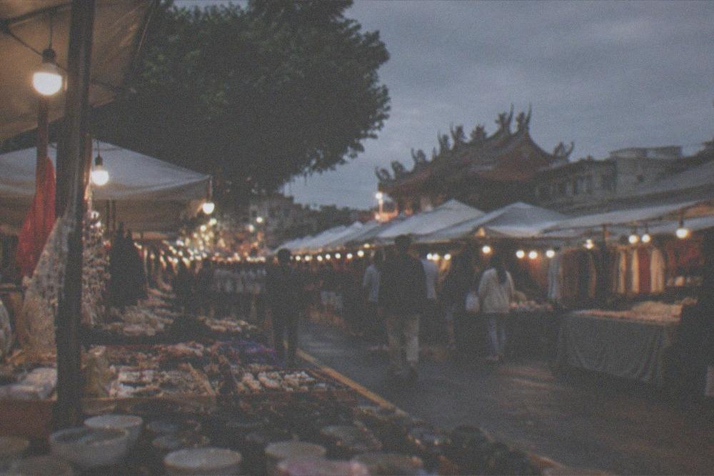 Crowded night market stalls lit by strings of bulbs at dusk