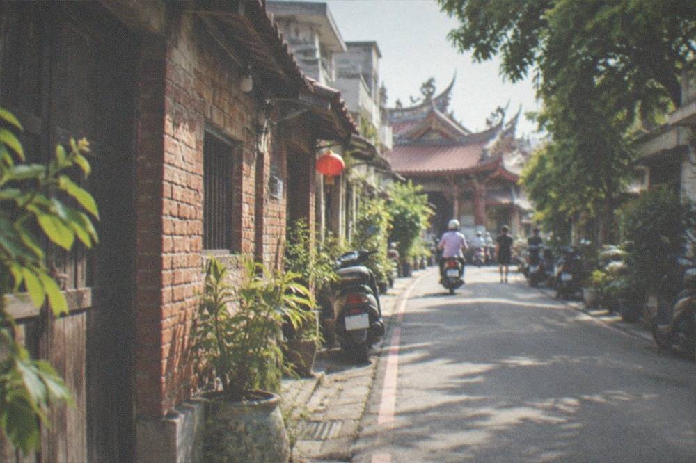 A narrow village lane in rural Taiwan with old brick walls, wooden doors and potted plants