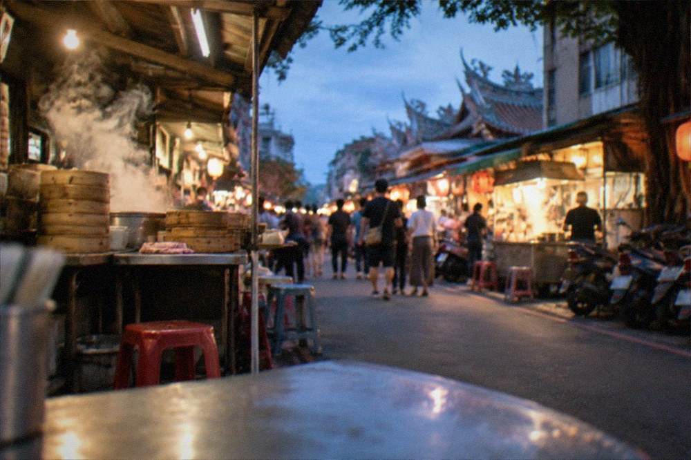 A lit-up Tainan food street at night with crowds walking between illuminated stalls