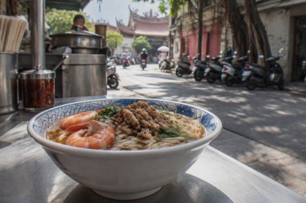 A small bowl of danzai noodles with shrimp and minced pork on a street food stall counter