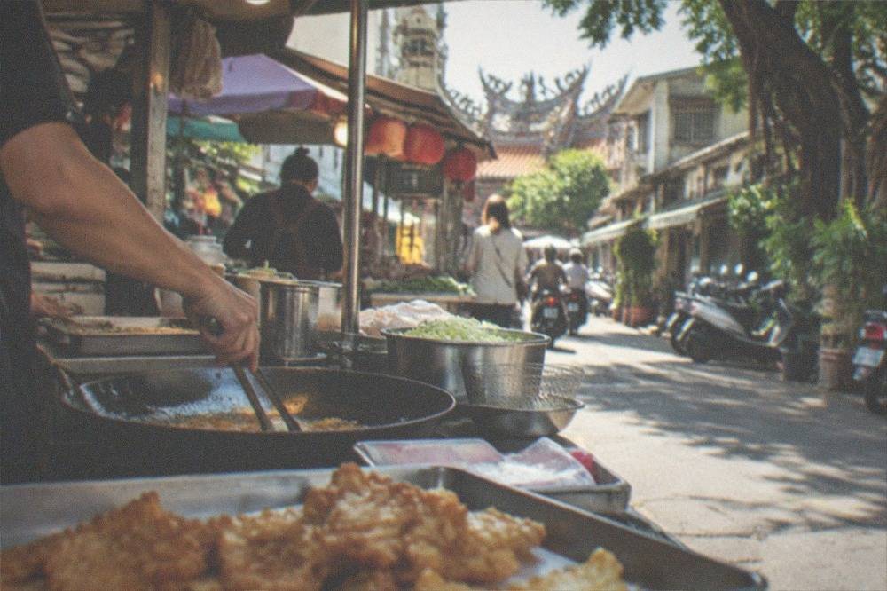 A row of small food stalls along an old street with vendors preparing dishes at counters