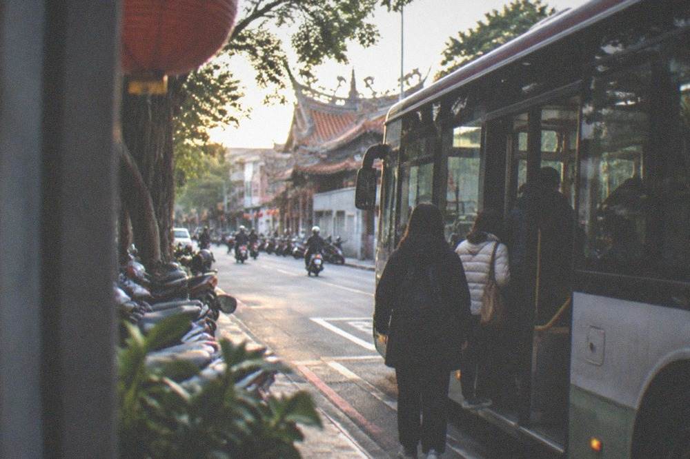 A city bus at a stop on a Tainan street with passengers boarding in the evening