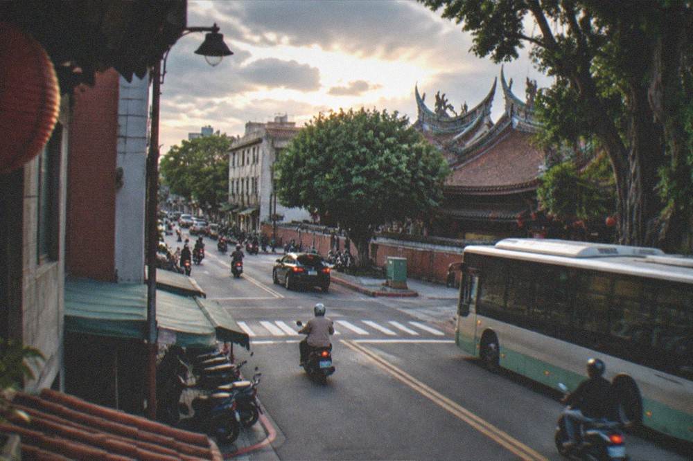 A street corner in Tainan's old city at dusk with buses and scooters passing