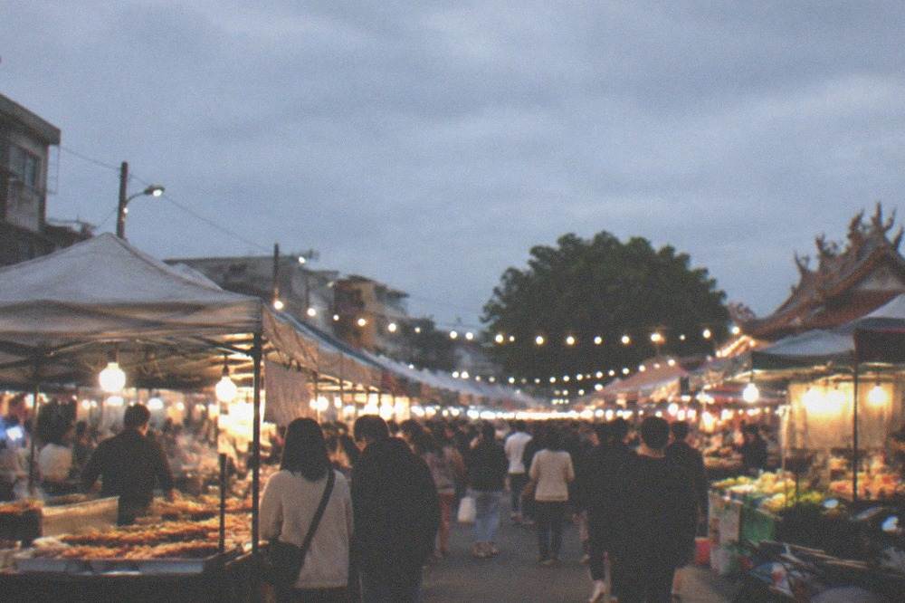 A busy night market stall in Tainan with food displayed and prices written on a Chinese signboard