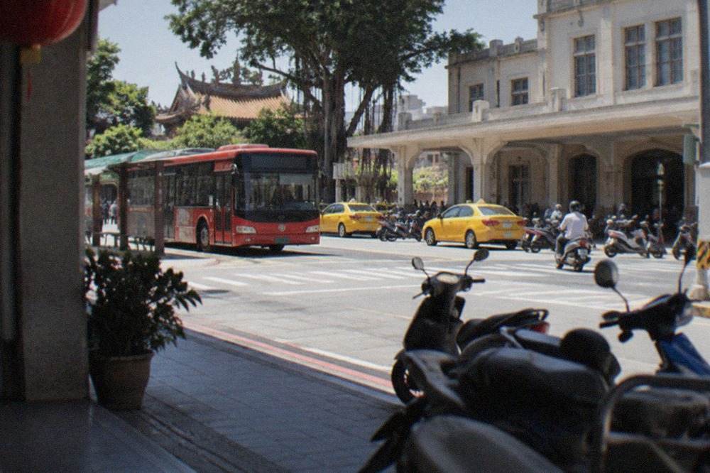 A red Tainan city bus stopped at a bus stop on a sunny street