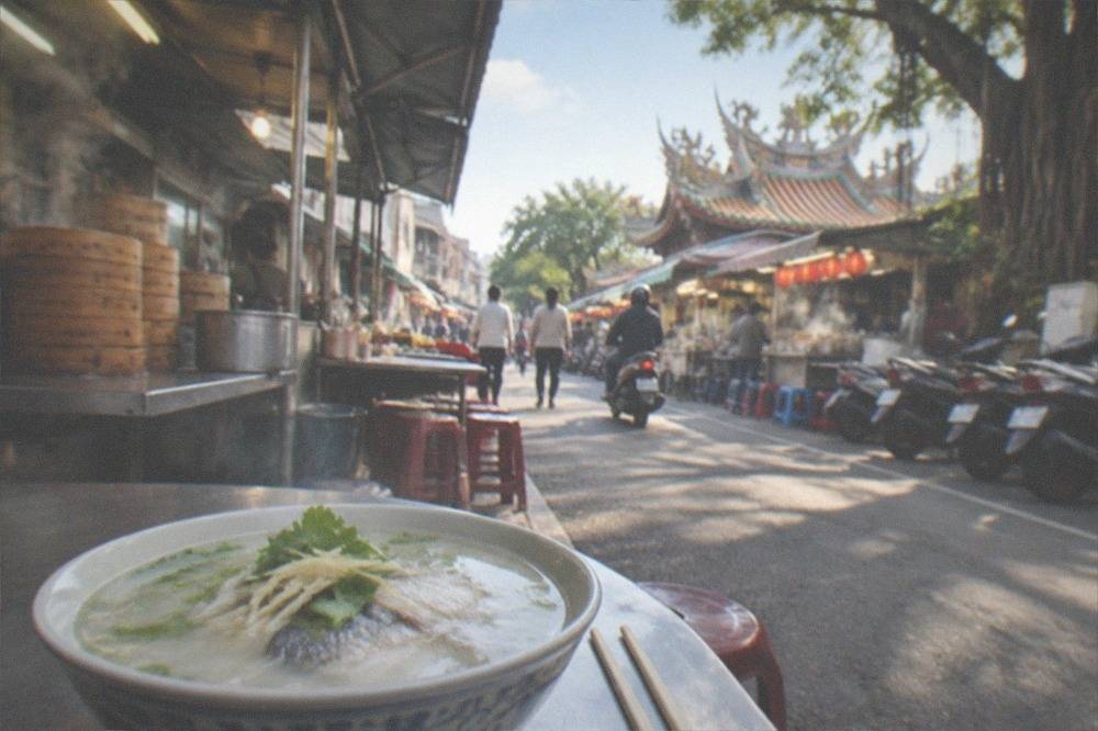 A bowl of milkfish porridge with ginger and celery leaves beside chopsticks