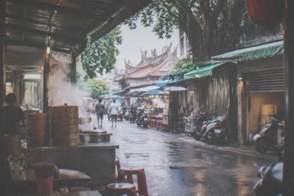 An early morning Tainan street with shop shutters opening and steam from a food stall