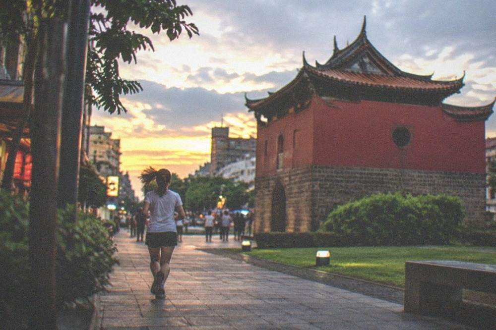 Red-walled historic tower with Chinese pavilion roofs in a city plaza at dusk