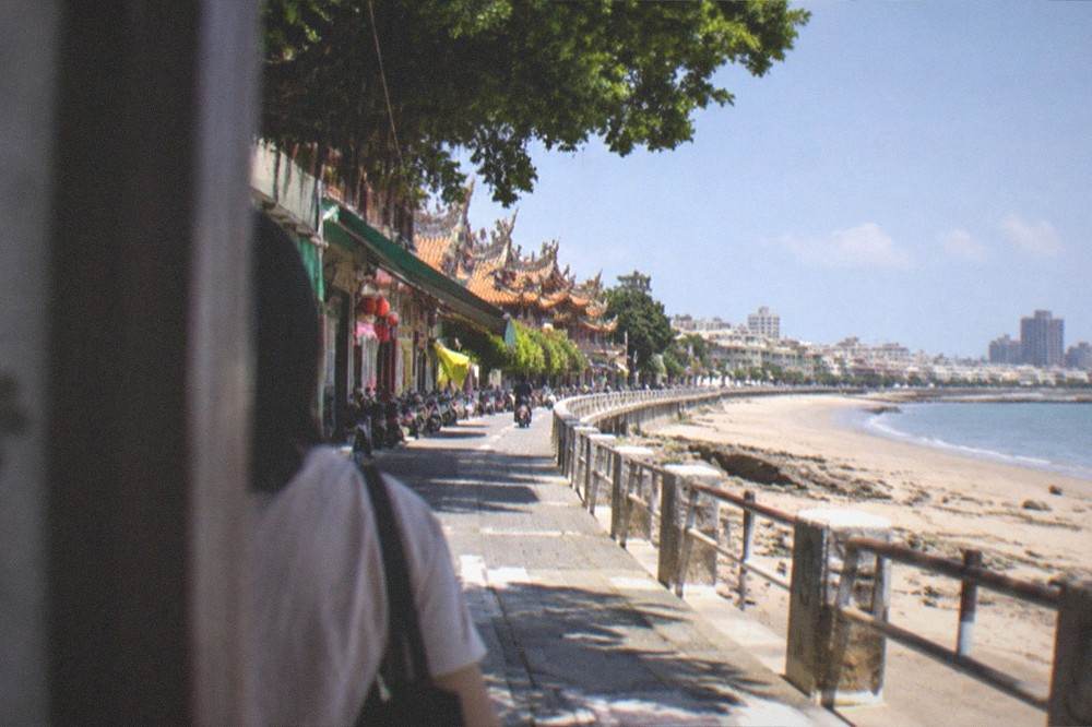 A long coastal path curving beside sand toward distant city buildings
