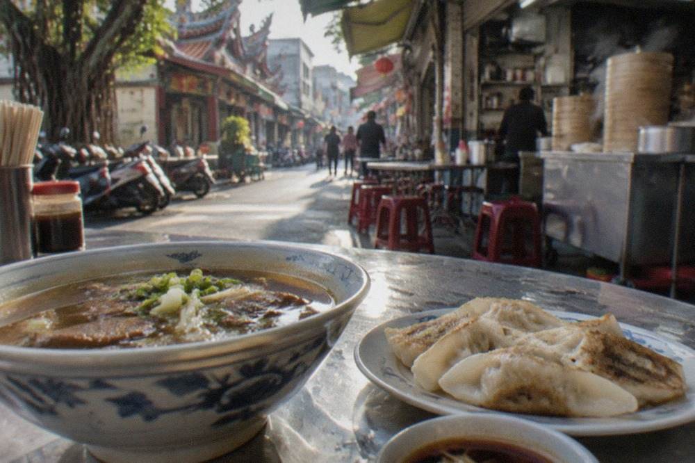 A bowl of Tainan beef soup beside a plate of breakfast dumplings on a small restaurant table