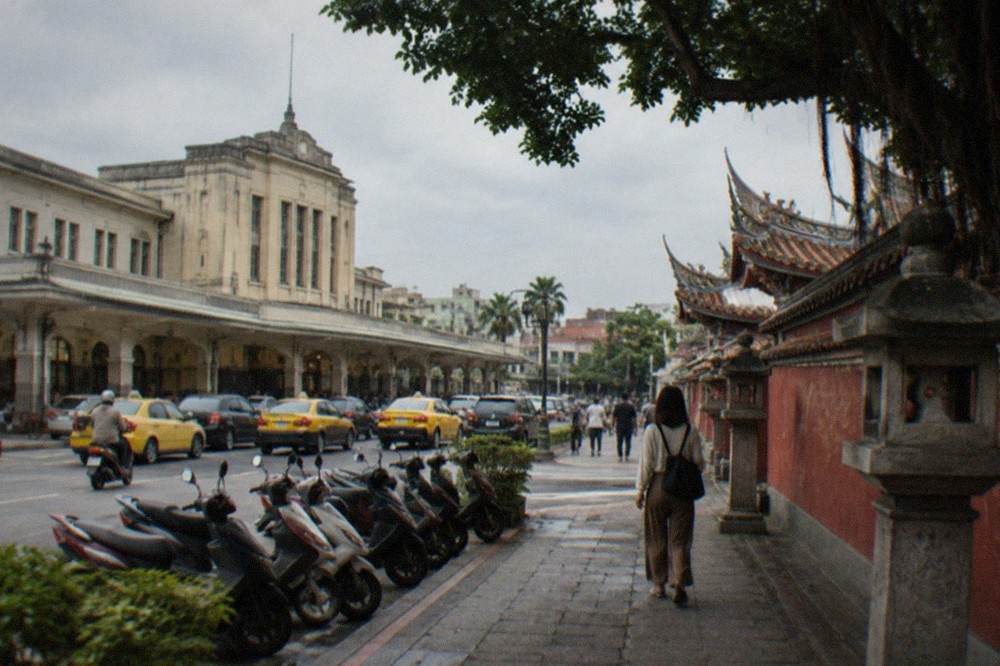 A visitor walking past red temple walls and stone lanterns in central Tainan