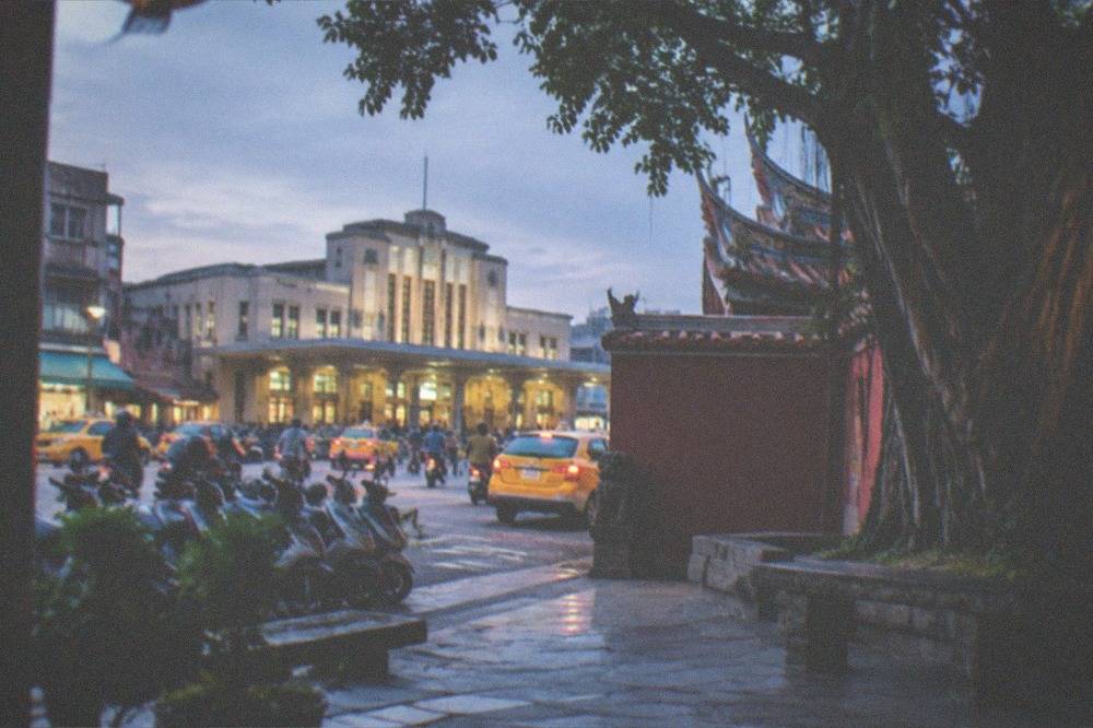 The courtyard of a Tainan temple with red walls, a banyan tree and stone benches