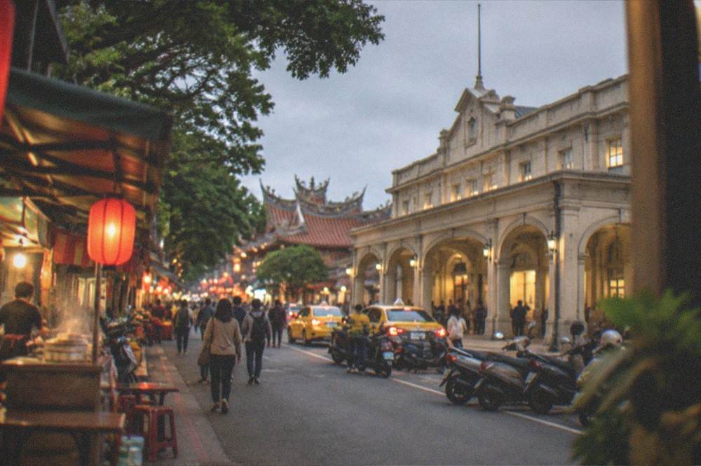 An old street lit warmly in the evening with food stalls and visitors walking