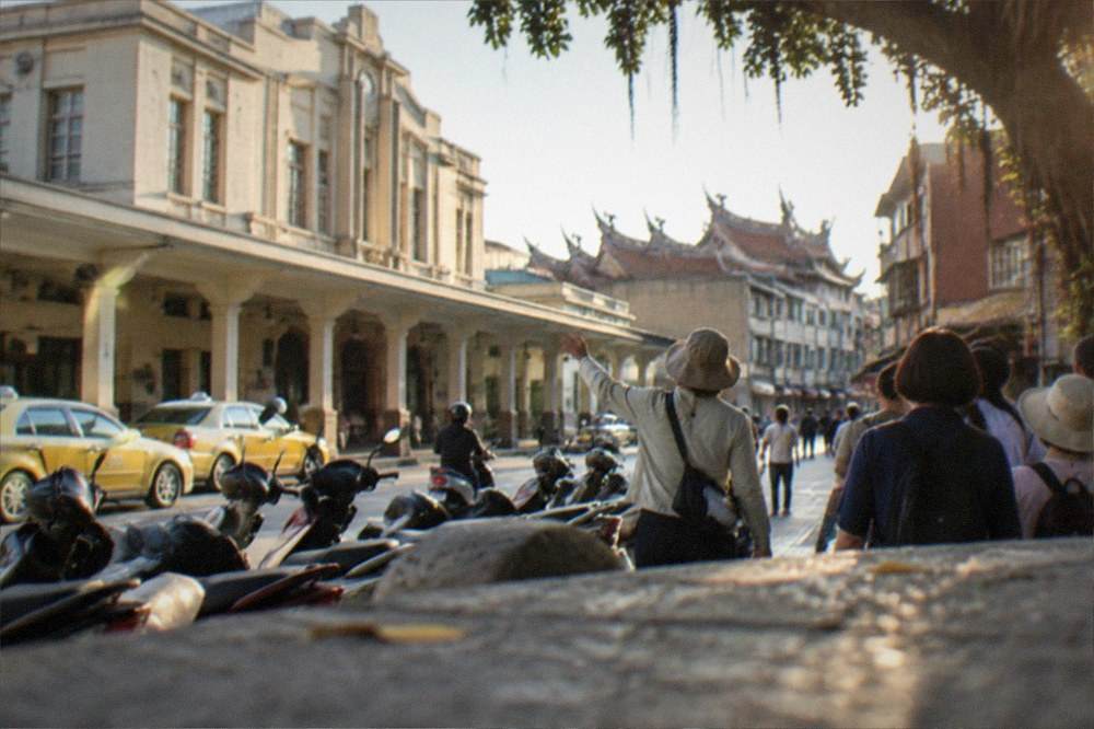 A guided tour group walking along a historic Tainan street with a guide gesturing toward an old facade