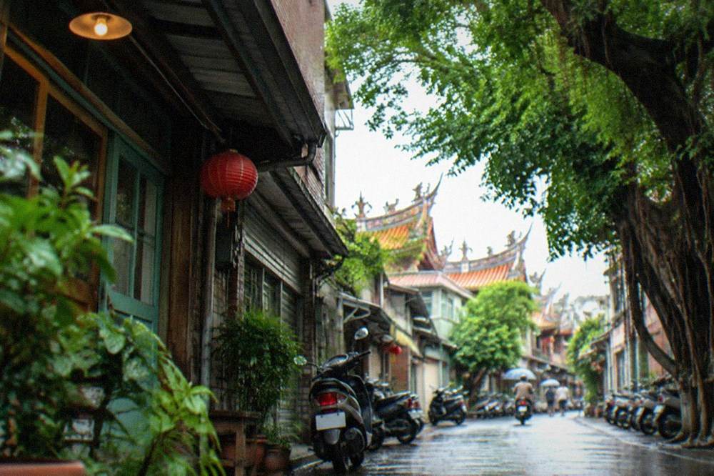 A narrow Tainan lane with old shophouses, a small cafe sign and scooters parked along the wall