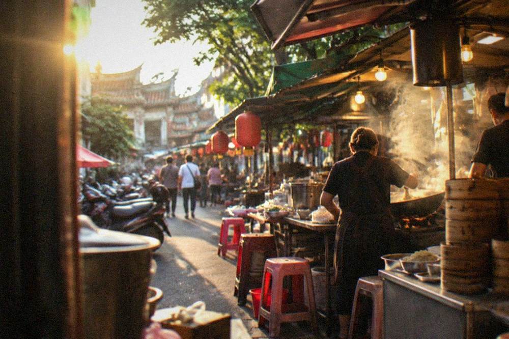 Stall vendors cooking noodles in woks at a crowded Tainan night market