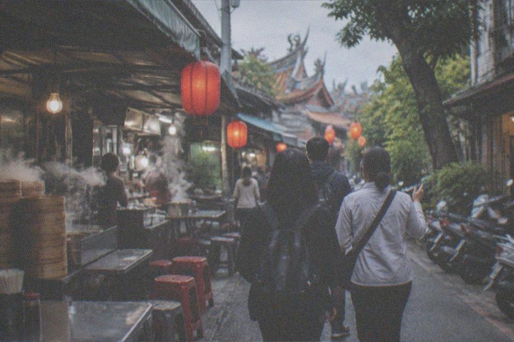 A small group of visitors walking with a guide down a lantern-lit Tainan alley