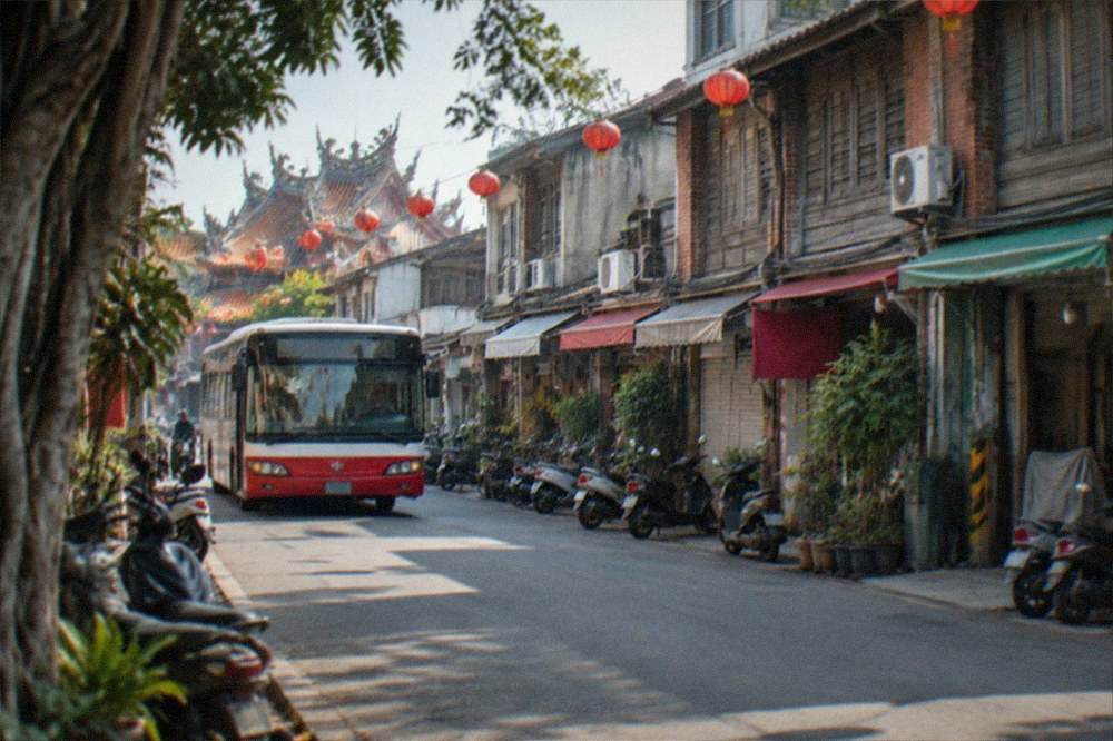 A red and white city bus at a stop on a sunny Tainan street