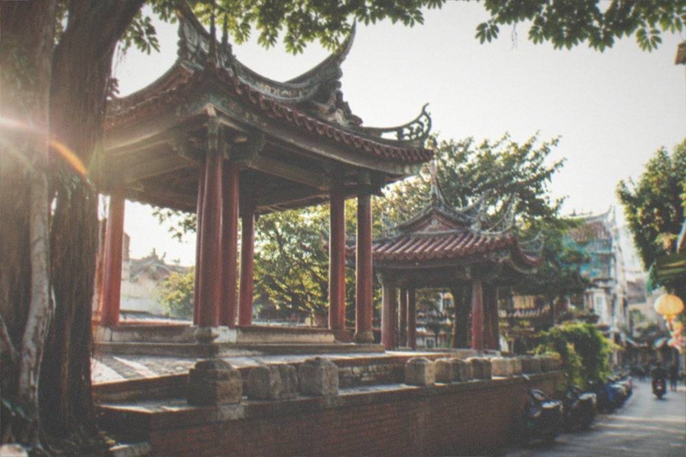 Pavilions with red columns and upswept roof ridges above a row of stone tablets on carved stone bases, the tablets seen edge on