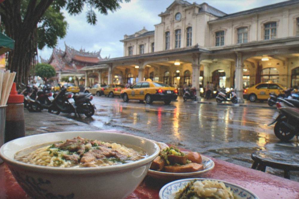 A bowl of Tainan noodles and side dishes on a small street food table at night