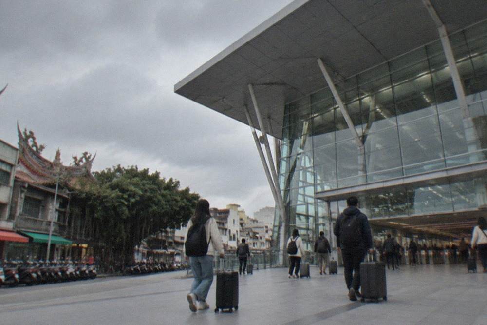A modern high speed rail station concourse with tall glass walls and travelers rolling suitcases toward the ticket gates