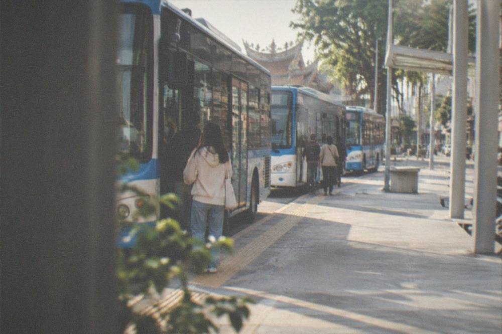 A row of blue and white city buses parked at a station kerb with passengers boarding