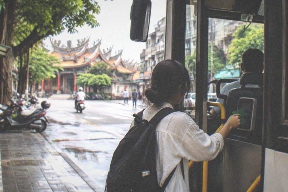 A traveler tapping a green fare card on a bus card reader beside the driver